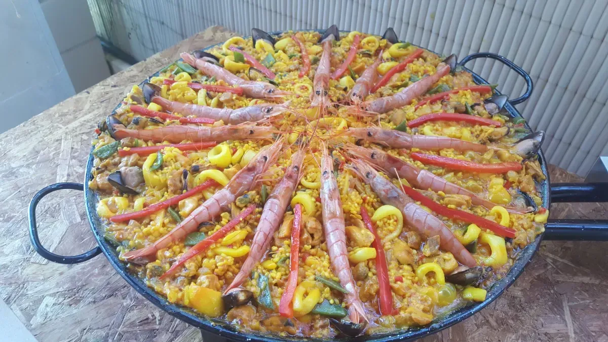 Una paellera grande con gambas y pimientos amarillos sobre la encimera.
