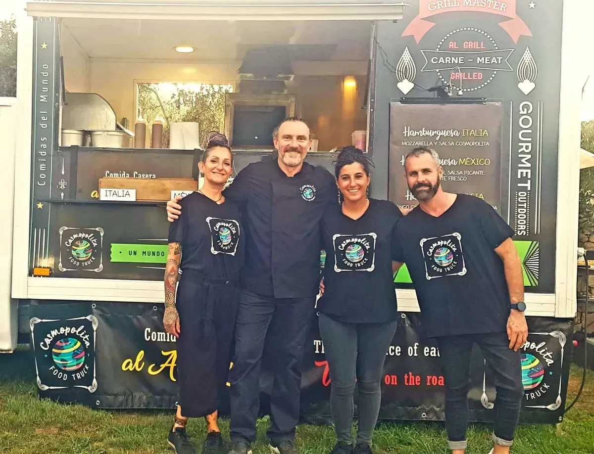 Cuatro personas con camisetas negras iguales posan sonrientes frente a un camión de comida al aire libre en un evento.