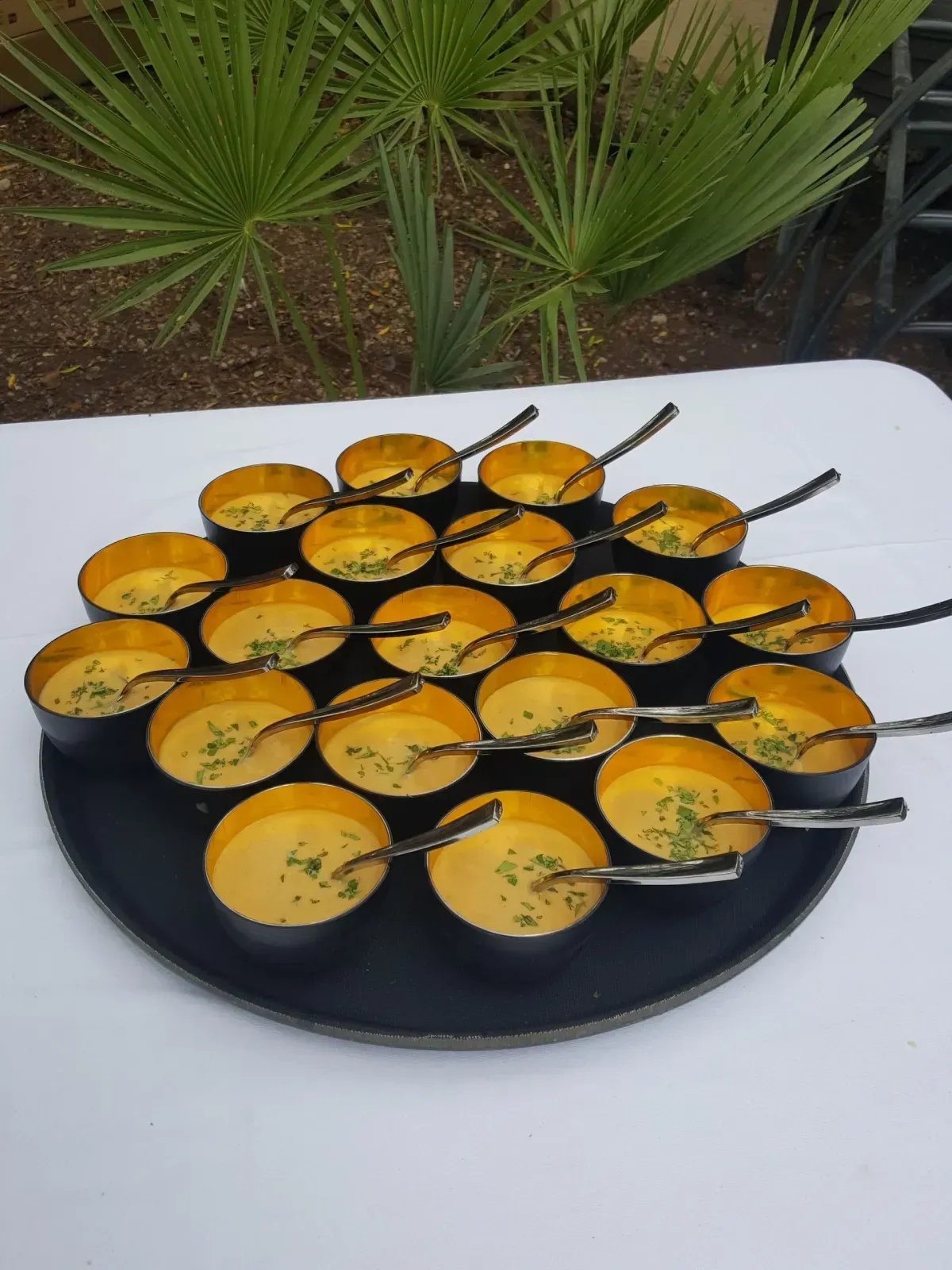 Bandeja negra con tazas pequeñas llenas de sopa de naranja, adornadas y con cucharas encima