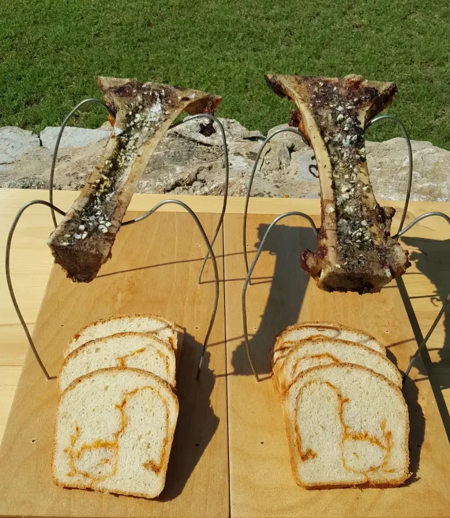 Rebanadas de pan debajo de dos trozos de carne a la parrilla colgando al aire libre.