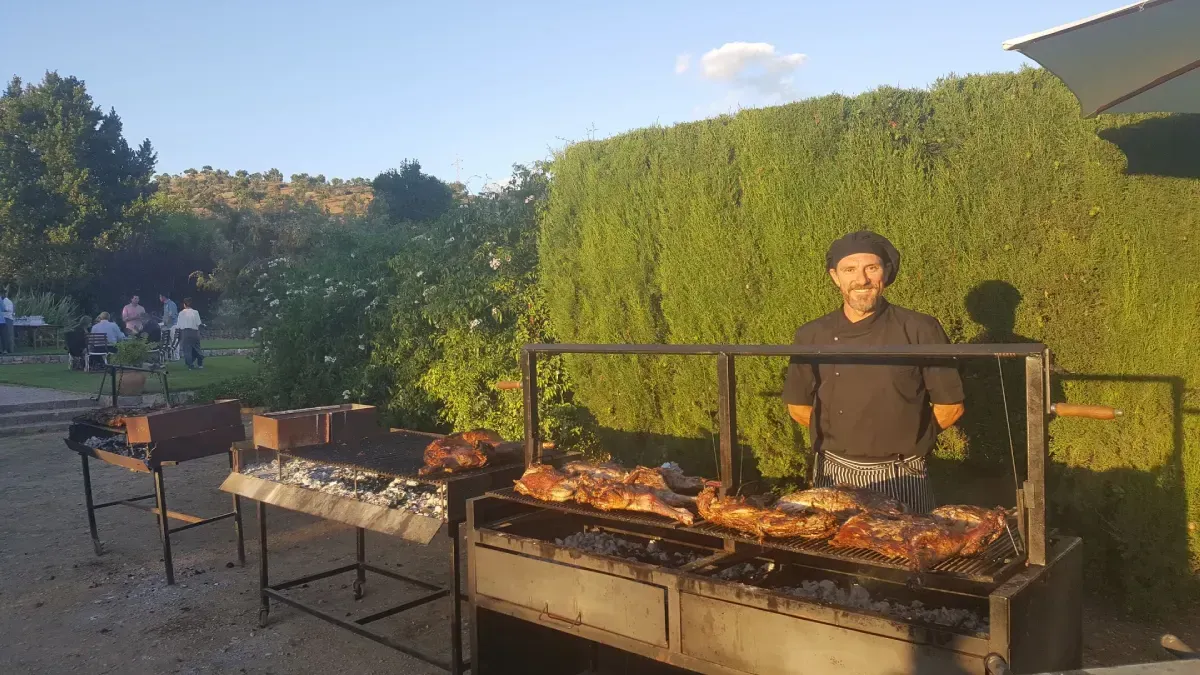 Una persona asa carne al aire libre junto a un largo seto al atardecer.