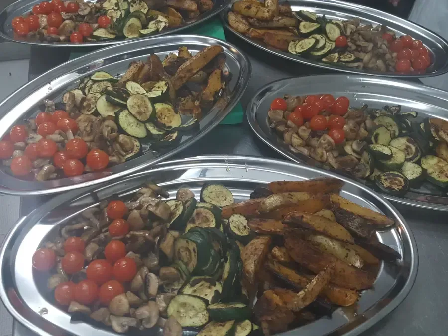 Bandejas de verduras a la parrilla y tomates cherry dispuestas en una mesa de bufé.