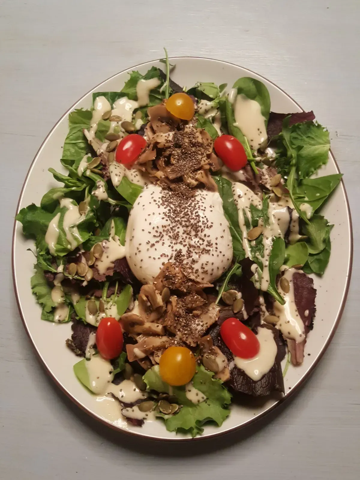 Ensalada emplatada con hojas verdes, burrata, tomates cherry, frutos secos y aderezo balsámico.
