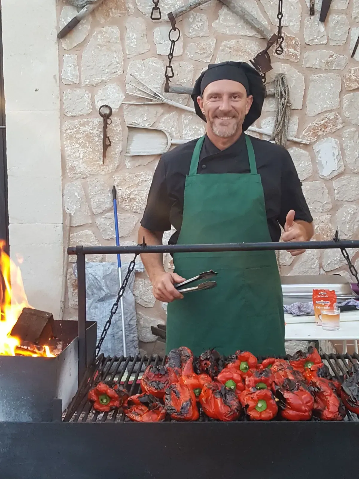Asando brochetas y pimientos a la parrilla sobre el fuego, con un cocinero sonriente con delantal verde