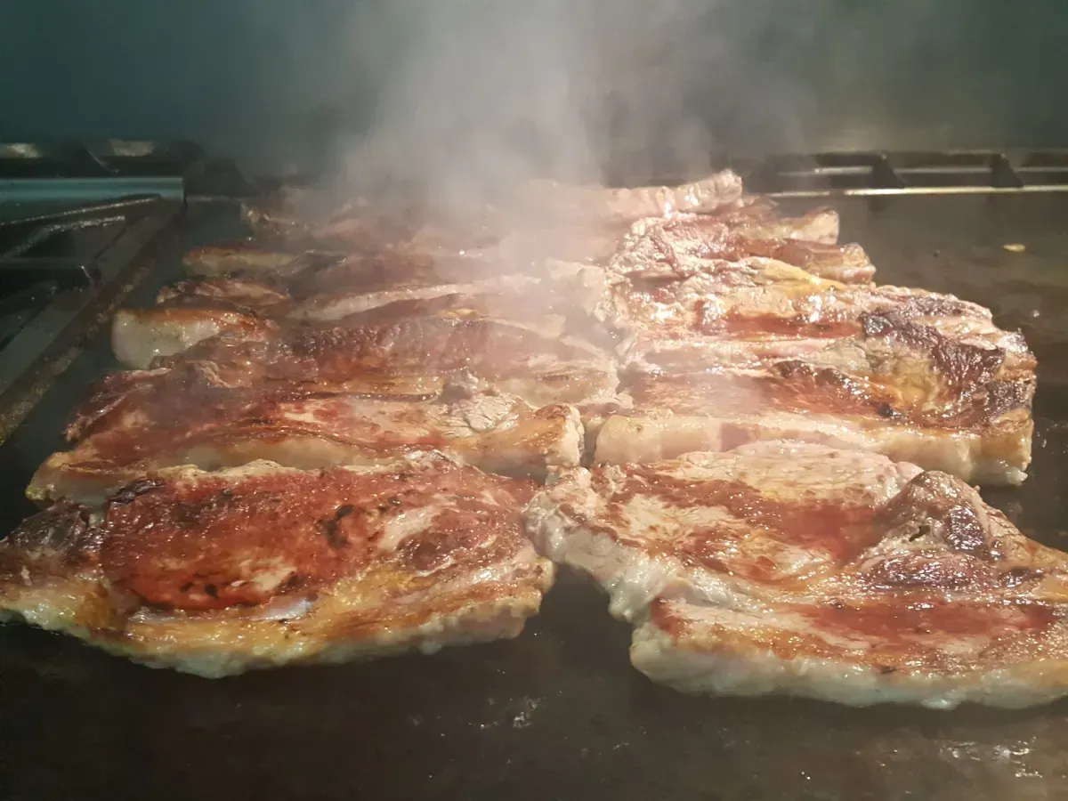 Filetes chisporroteando en la parrilla con humo que se eleva y superficies doradas y selladas.