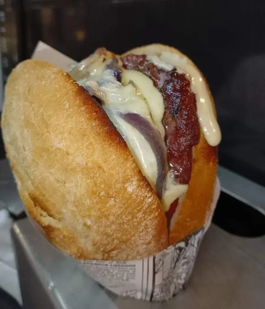 Sándwich de tocino y queso en un pan crujiente, envuelto en papel.