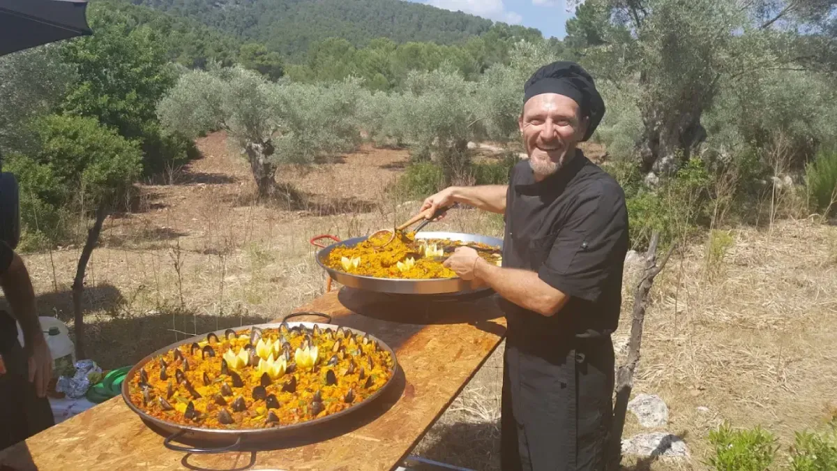 Una persona vestida de negro sostiene una bandeja con flores naranjas junto a una mesa llena de flores