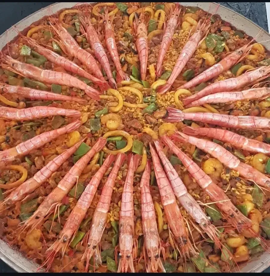 Arroz con azafrán cubierto con camarones dispuestos en círculo y pimientos esparcidos en una sartén grande.
