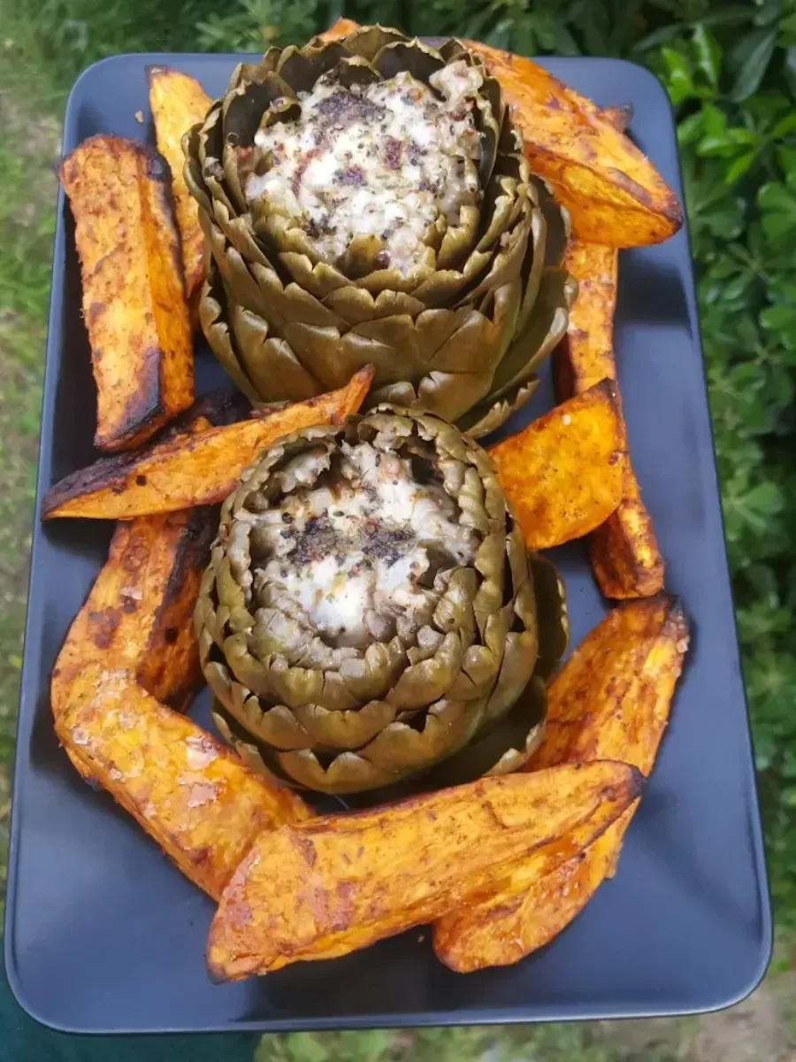 Alcachofas asadas cubiertas de queso, acompañadas de patatas gajo sazonadas en un plato azul.