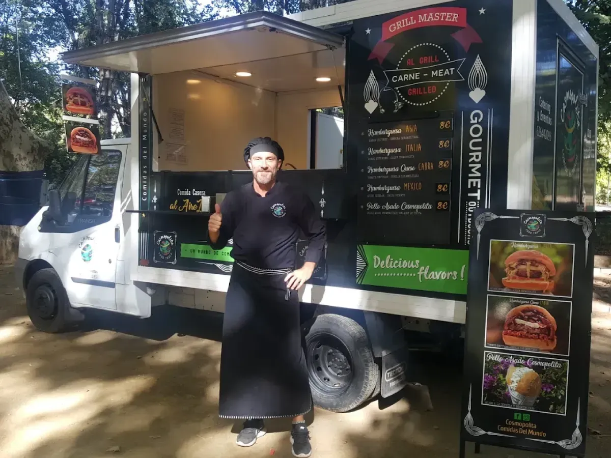 Camión de café con ventanilla de servicio abierta, carteles con el menú y una persona de pie afuera sosteniendo una bebida.
