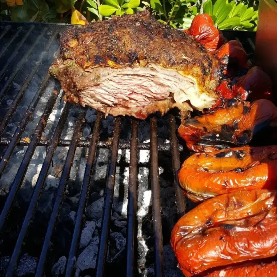 Primer plano de carne asada y pimientos rojos chisporroteando sobre las brasas en una parrilla.