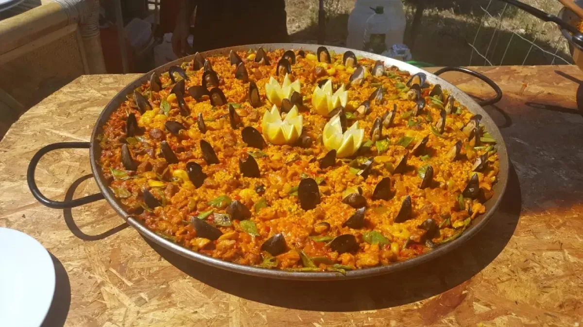 Una gran paella con arroz, gambas, mejillones y rodajas de limón sobre una mesa.