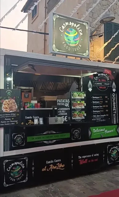 Quiosco de comida callejera con toldo negro, pizarras con menús y un letrero de neón