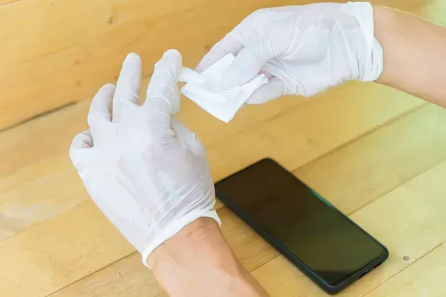 Una persona con guantes blancos está limpiando un teléfono celular en una mesa de madera.