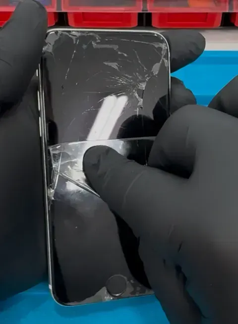 Una persona que lleva guantes negros sostiene un teléfono celular con la pantalla rota.