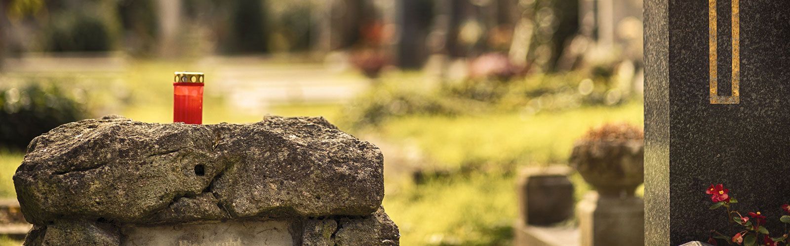 Auf einem Felsen auf einem Friedhof steht eine rote Kerze.