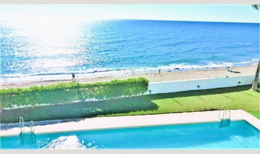 Hay una piscina en primer plano y una playa al fondo.