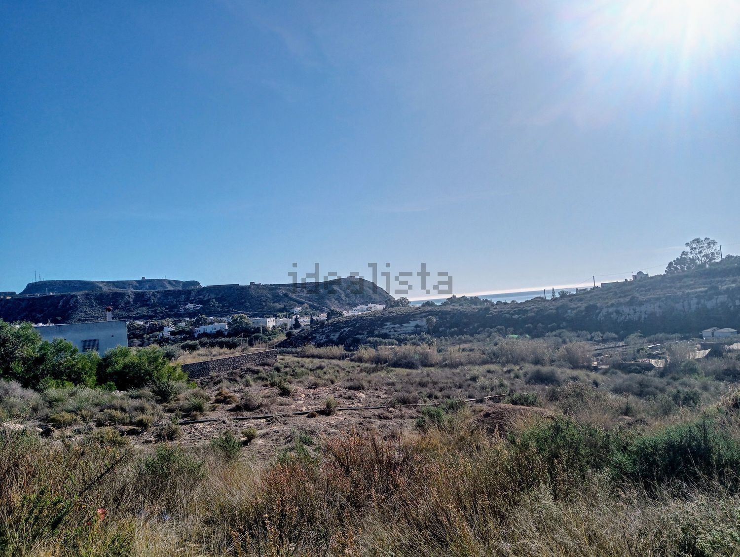 Un campo con un cielo azul y montañas al fondo.