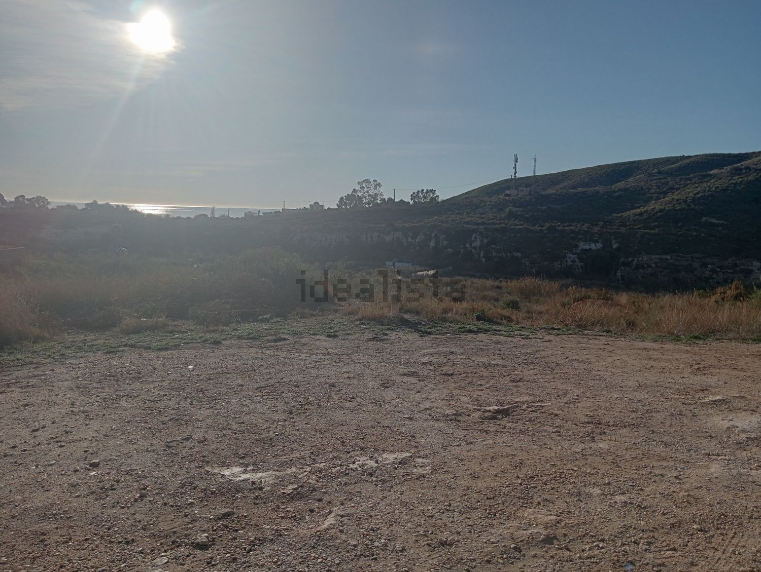 Un campo de tierra con una montaña al fondo y el sol brillando a través de las nubes.