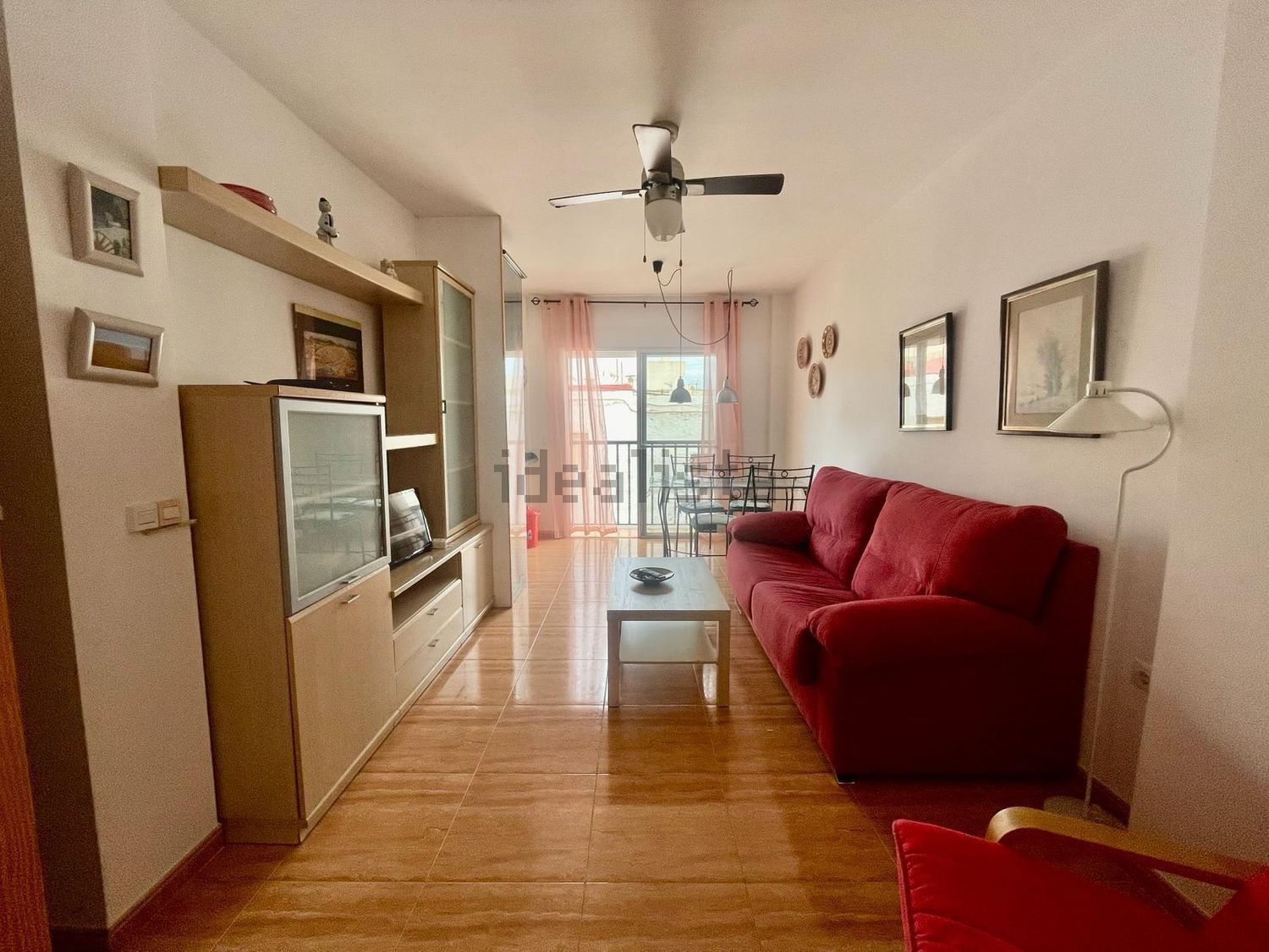 Una sala de estar con un sofá rojo y un ventilador de techo.