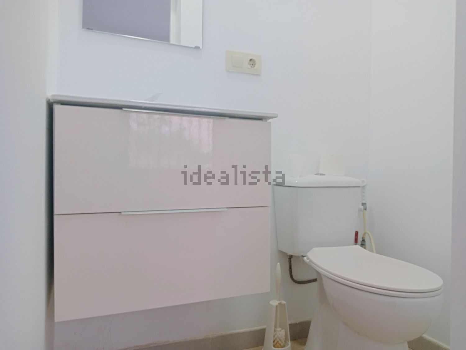Un baño con inodoro, lavabo, espejo e idealista escrito en la pared.