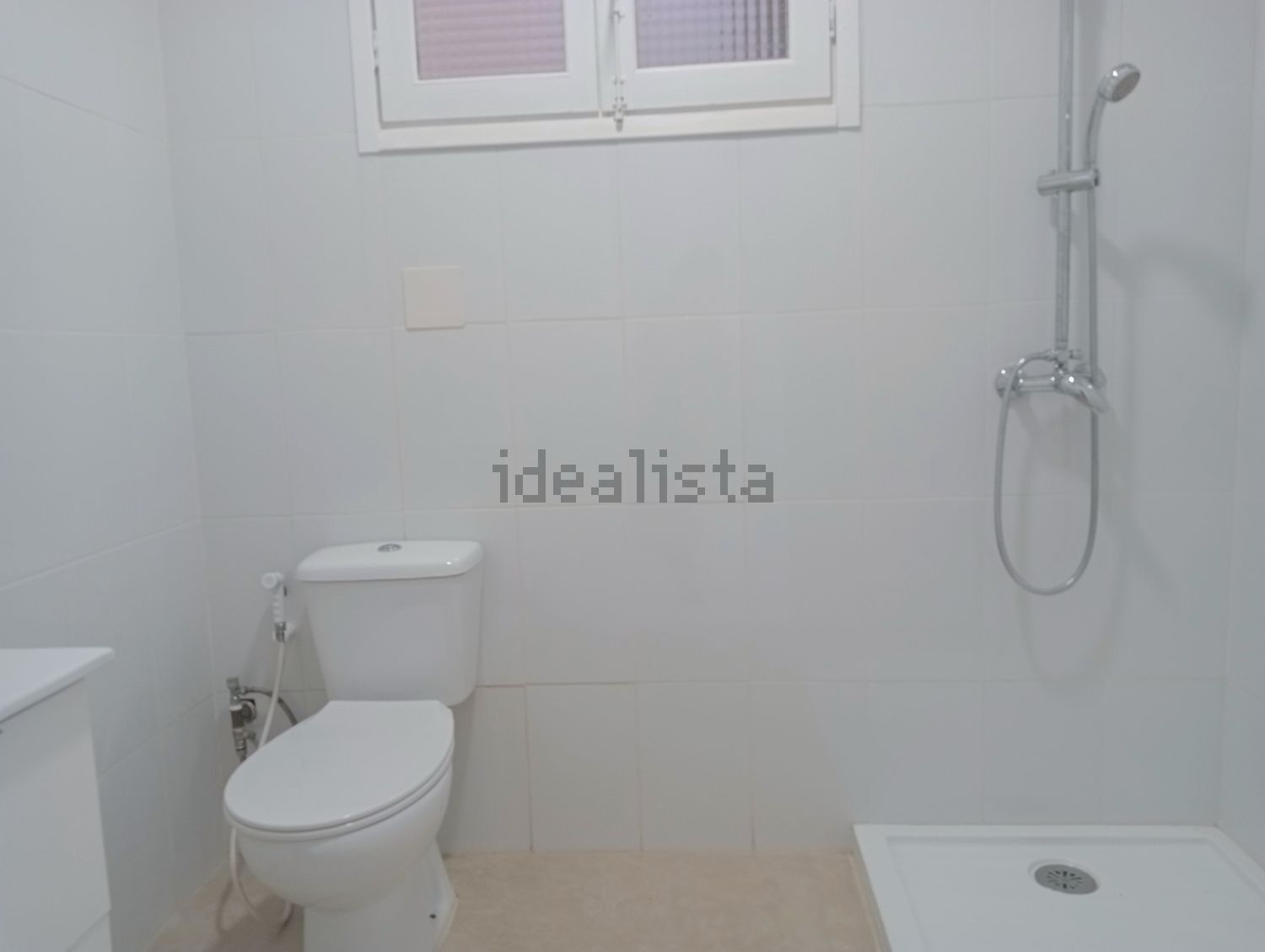 Un baño con inodoro, ducha y "Idealista" escrito en la pared.