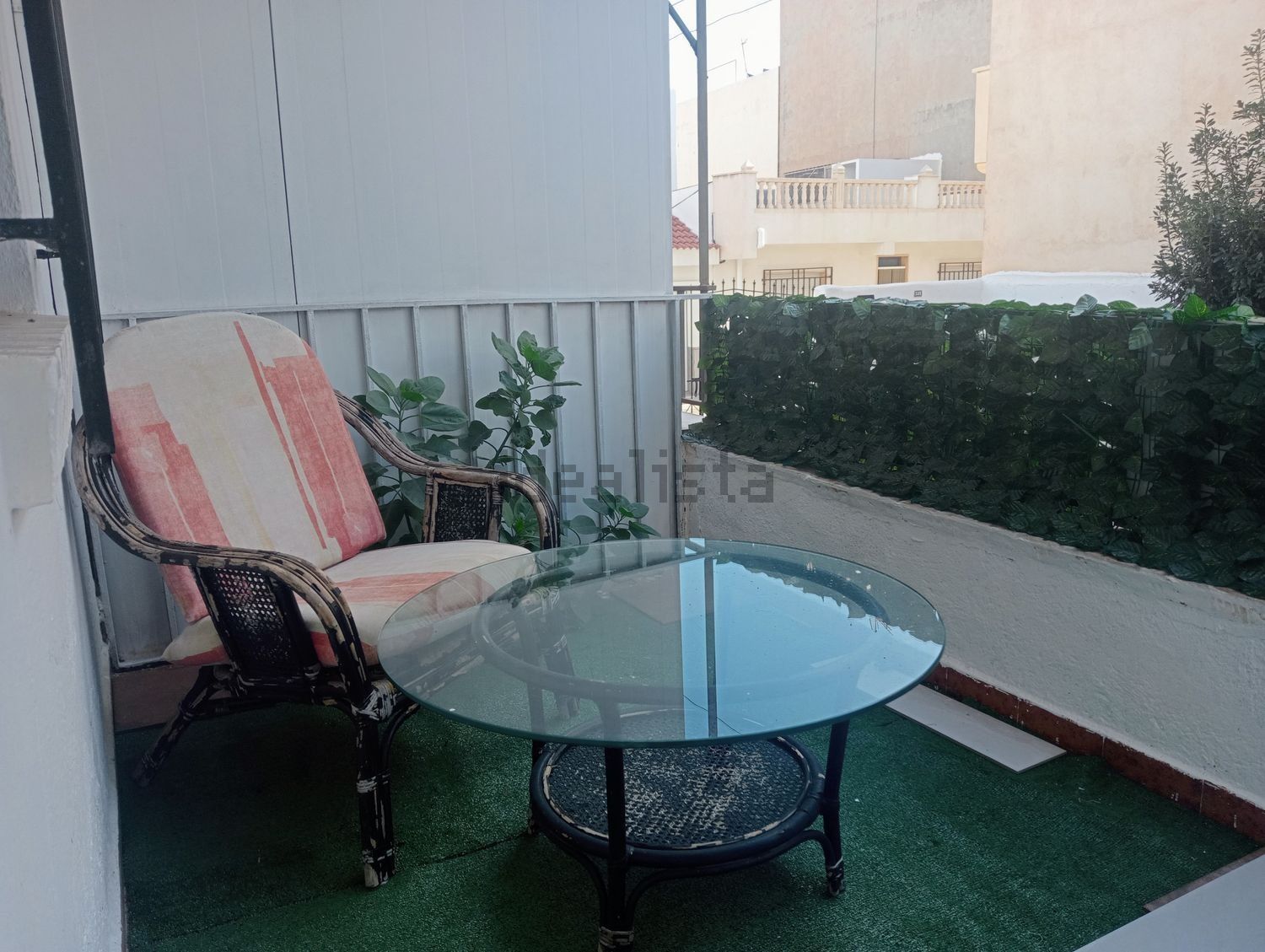 Un balcón con una silla de mimbre y una mesa de cristal.