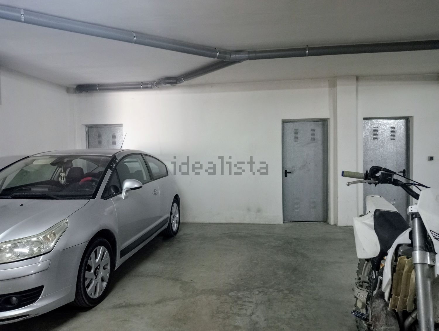 Un coche plateado está aparcado en un garaje junto a una motocicleta.