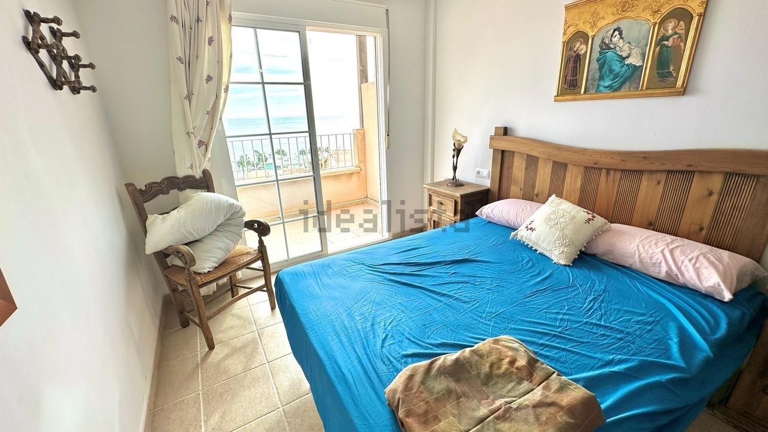 Un dormitorio con una cama, una silla, una mesita de noche y un cuadro en la pared.