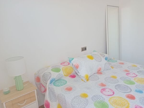 Un dormitorio con cama, mesita de noche, lámpara y espejo.