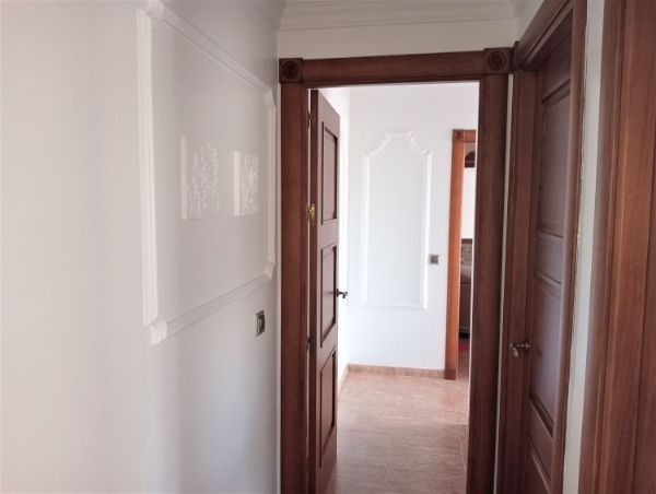 Un pasillo con una puerta de madera y paredes blancas.