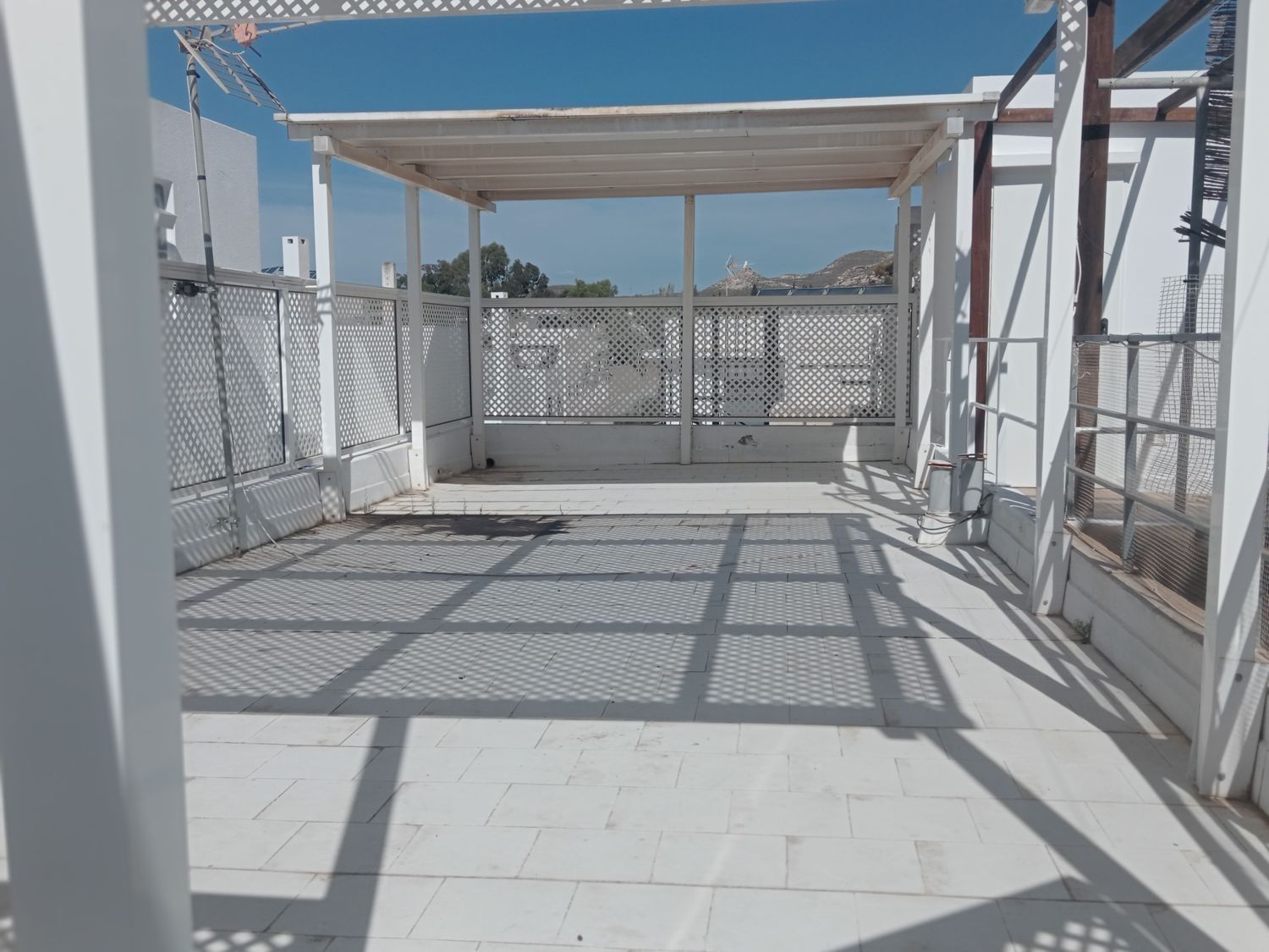 Un patio blanco con pérgola y sombras en el suelo.