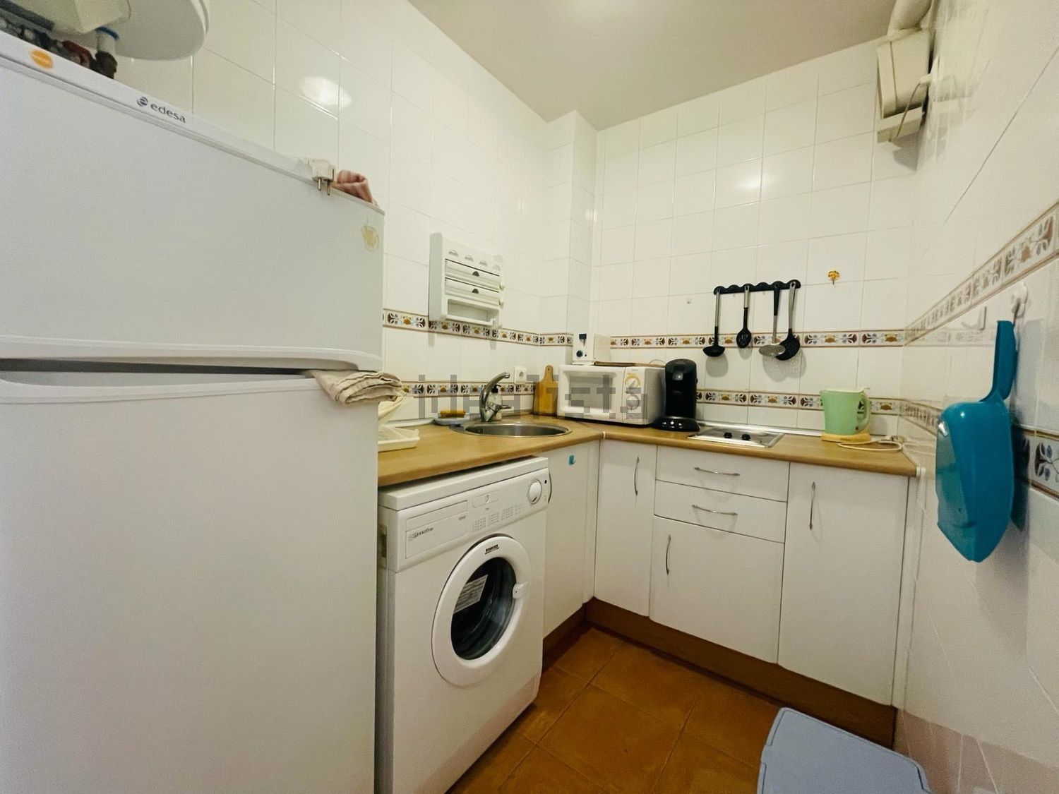 Una cocina con gabinetes blancos, una lavadora, un refrigerador y un microondas.