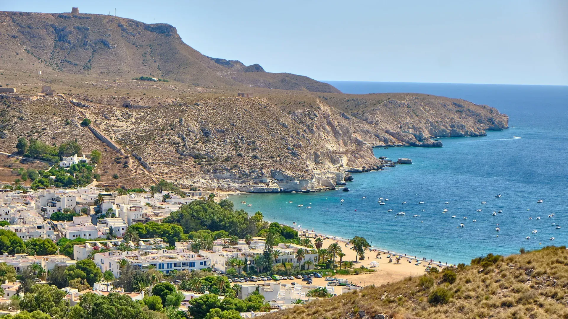 Una playa rodeada de montañas y árboles junto a un cuerpo de agua.