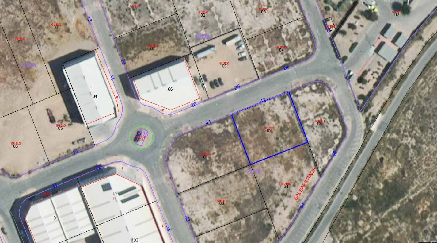 Vista aérea de una zona residencial con lotes vacíos, edificios, caminos y una rotonda.