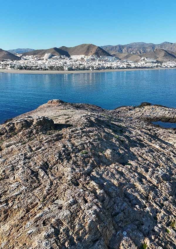 Un acantilado rocoso con vistas a un cuerpo de agua con montañas al fondo.