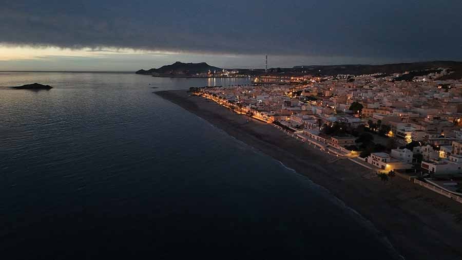 Una vista aérea de una playa de noche con una ciudad al fondo.