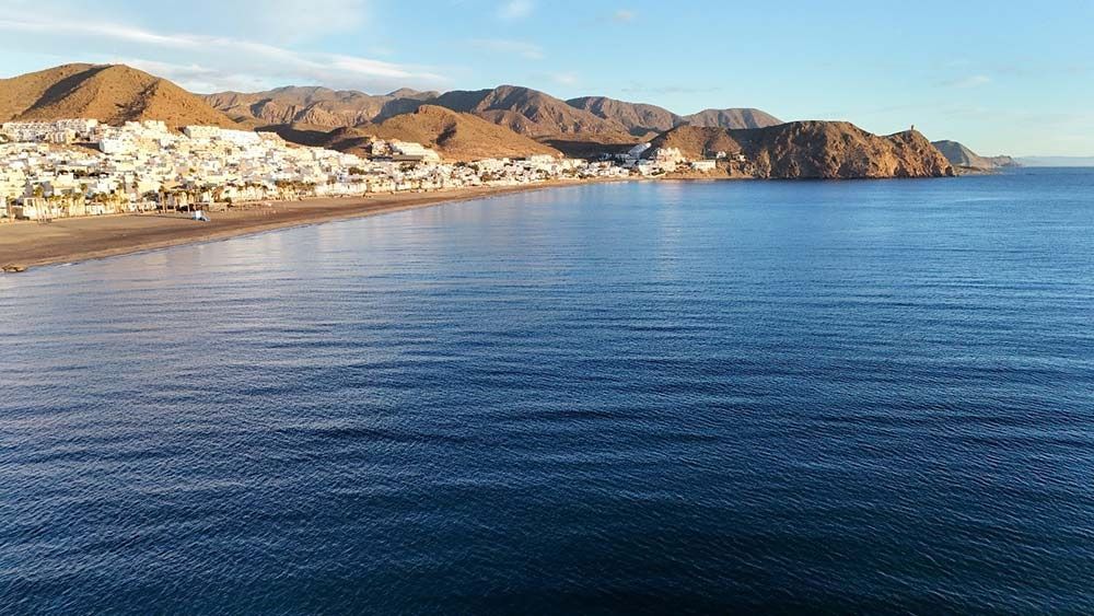 Una gran masa de agua con montañas al fondo y una playa en primer plano.