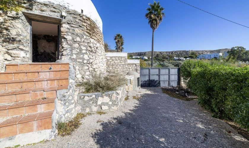 Un camino de tierra que conduce a un edificio de piedra con una palmera al fondo.