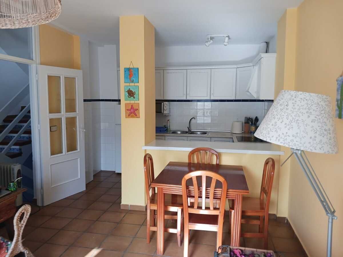 Comedor con mesa y sillas, que conduce a una cocina con gabinetes blancos.