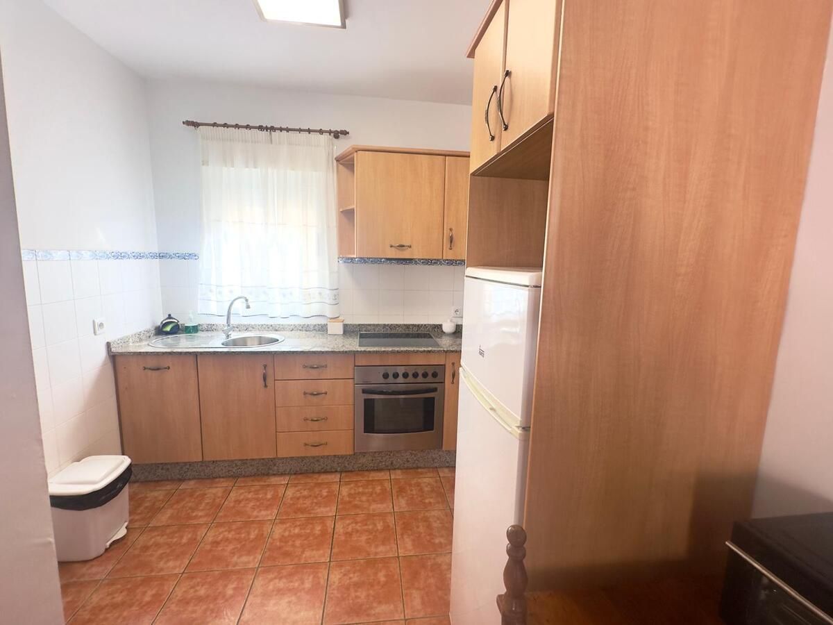 Pequeña cocina con gabinetes de madera, fregadero de acero inoxidable, horno y microondas cerca de una ventana.