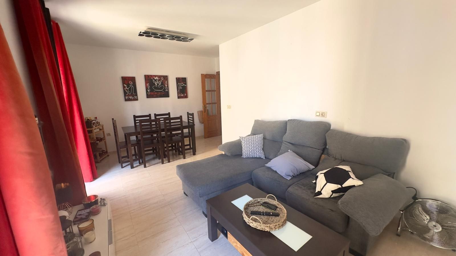 Pequeña cocina con encimera, gabinetes, refrigerador, mesa con frutas y una puerta de entrada.