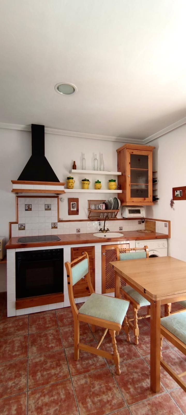 Una cocina rústica con gabinetes de madera y una mesa, sillas y piso de baldosas rojas.