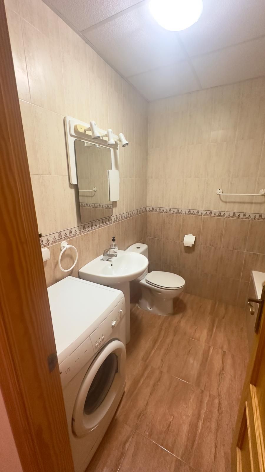 Interior de apartamento pequeño con cocina, mesa de comedor, sofás azules, obras de arte y ventilador de techo.