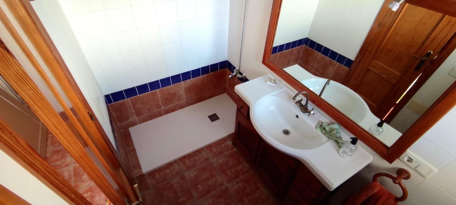 Una cocina rústica con gabinetes de madera y una mesa, sillas y piso de baldosas rojas.