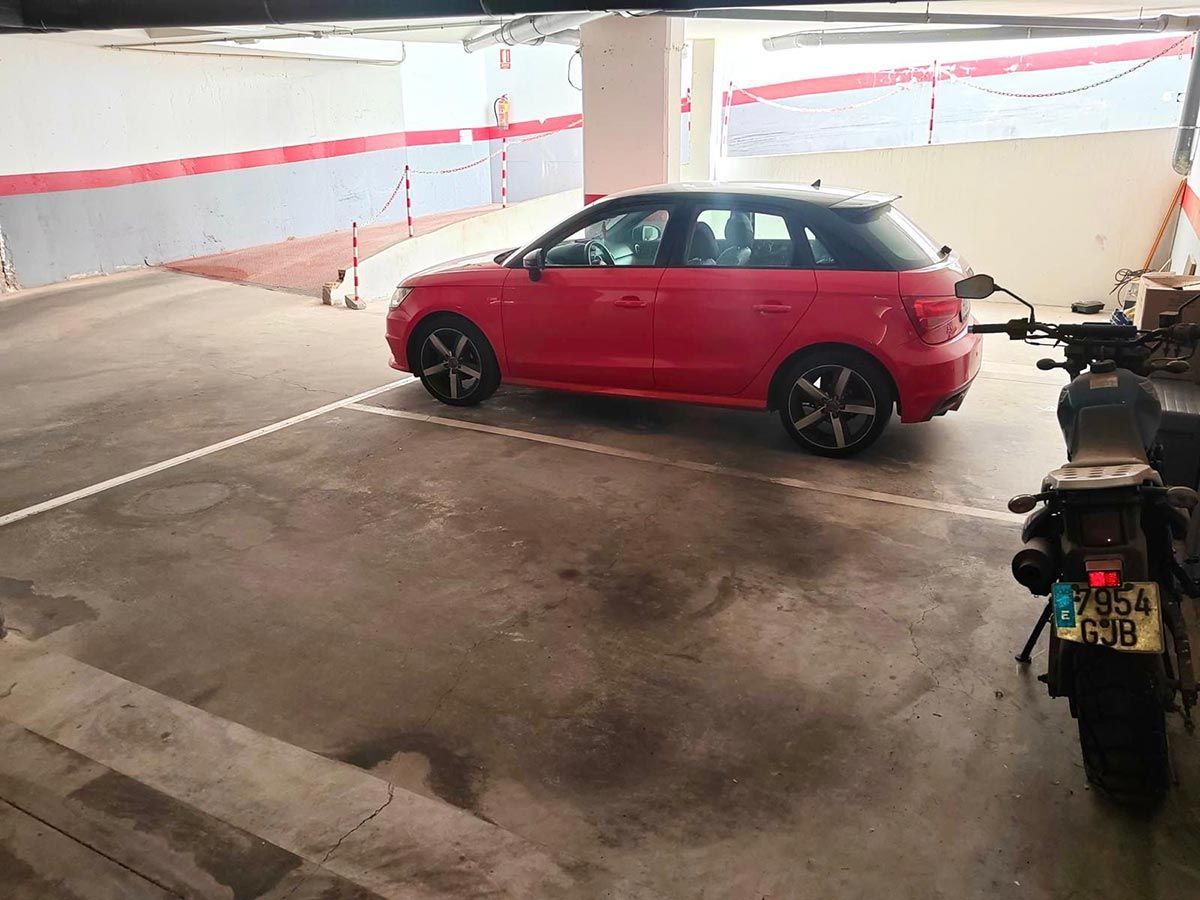 Baño estrecho con inodoro blanco, lavabo oscuro y ducha de cristal. Suelo gris, azulejos beige y paredes blancas.