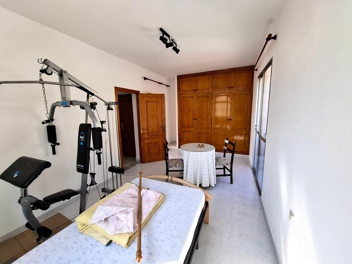 Gimnasio en casa con equipo de entrenamiento, una mesa de masajes y una mesa pequeña y sillas.