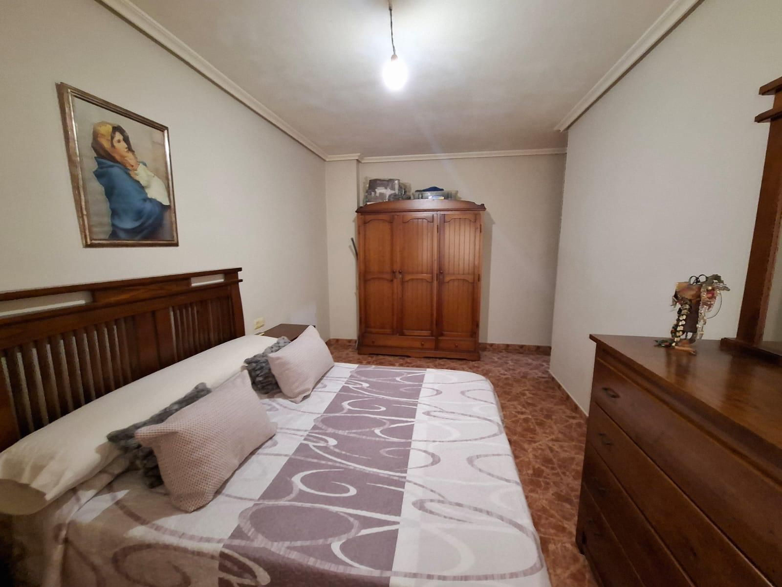 Dormitorio con cama, armario blanco y puerta abierta a un pasillo. Ventilador de techo rojo.