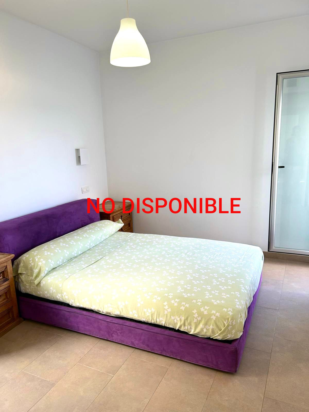 Cama morada con sábanas estampadas en verde claro, dos mesitas de noche de madera, paredes blancas y una puerta de vidrio esmerilado.