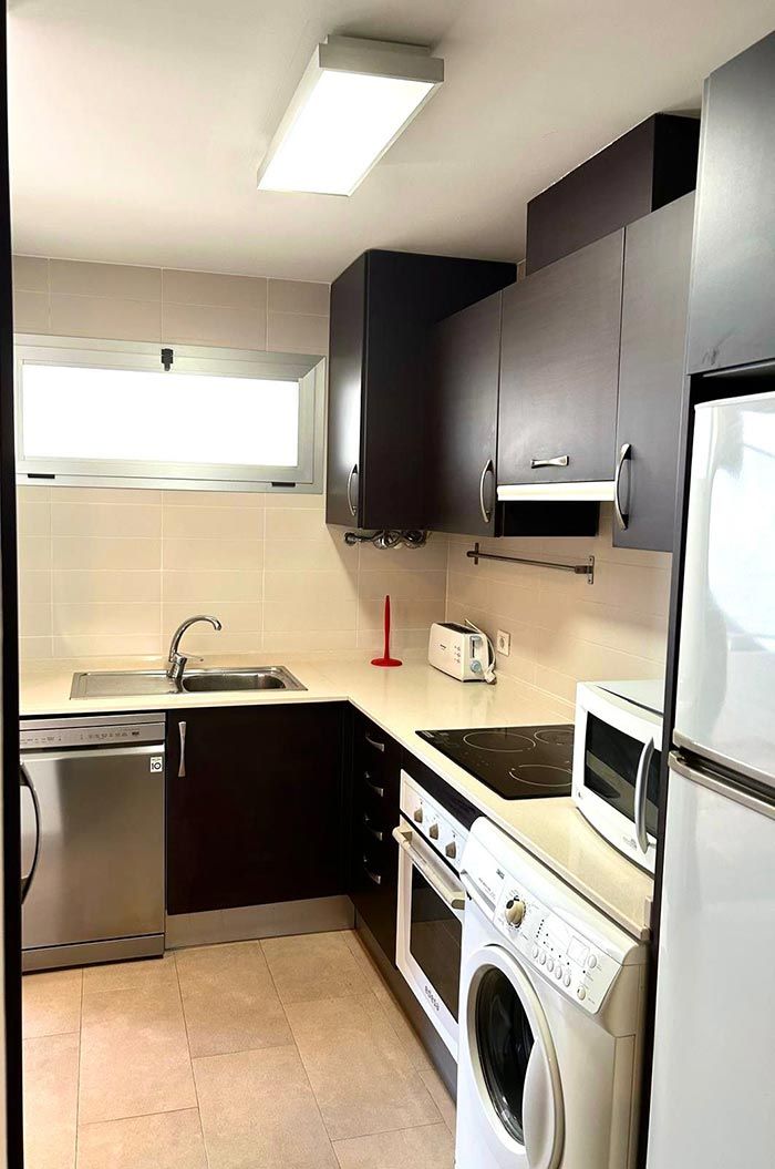 Cama morada con sábanas estampadas en verde claro, dos mesitas de noche de madera, paredes blancas y una puerta de vidrio esmerilado.